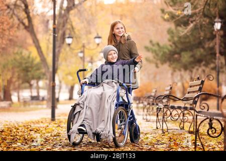 Little boy in wheelchair with sister outdoors Stock Photo