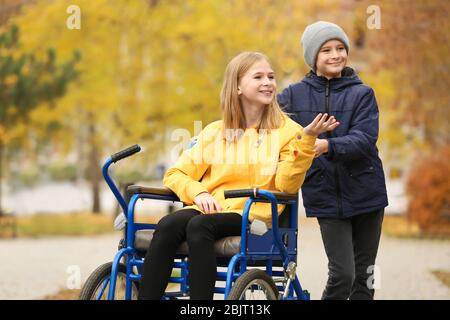 Little girl in wheelchair with brother outdoors Stock Photo