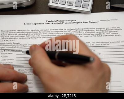 A U.S. government Paycheck Protection Program loan application form is shown up close, with a hand holding an ink pen about to fill out the paperwork. Stock Photo