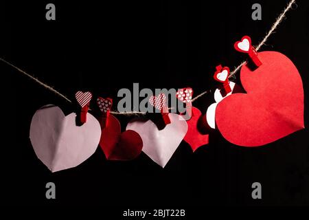 Paper hearts of red clothespins with a heart on a rope. Valentine's day love. Black background. copy space Stock Photo