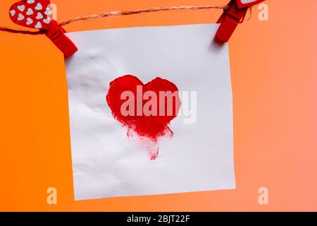 a piece of paper with a patterned heart of fingerprints of red clothespins with a heart on a rope. Valentine's Day love. Lush Lava Background. copy sp Stock Photo