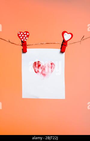 a piece of paper with a patterned heart of fingerprints of red clothespins with a heart on a rope. Valentine's Day love. Lush Lava Background. copy sp Stock Photo