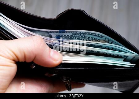 a bundle of hundred-dollar banknote in a black leather wallet in his hand. view from the side. close up Stock Photo