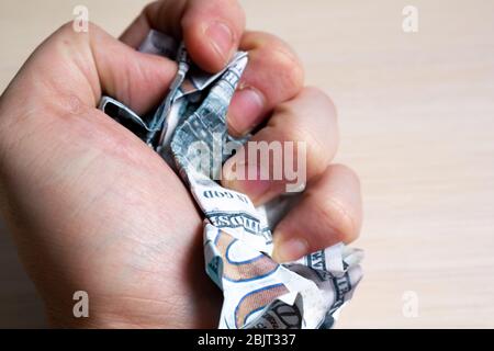 Hand squeezes hundred dollar bills on a light wooden table. side view. to close Stock Photo
