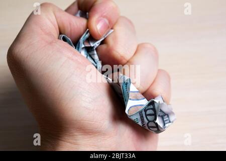 Hand squeezes hundred dollar bills on a light wooden table. side view. to close Stock Photo