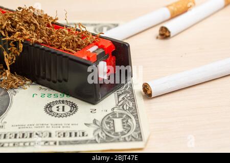 machine for filling cigarettes with tobacco and cigarettes and a dollar on  a light tree Stock Photo