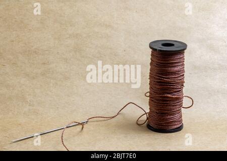 brown thread with a needle on a cardboard background Stock Photo