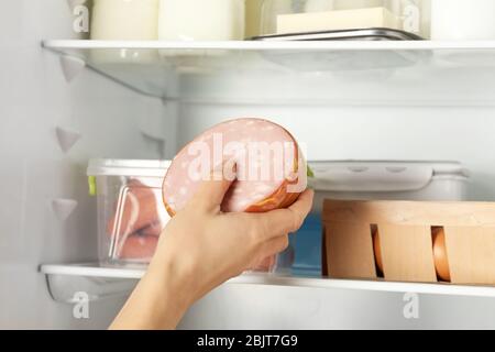 Young woman taking yummy sausage from refrigerator Stock Photo