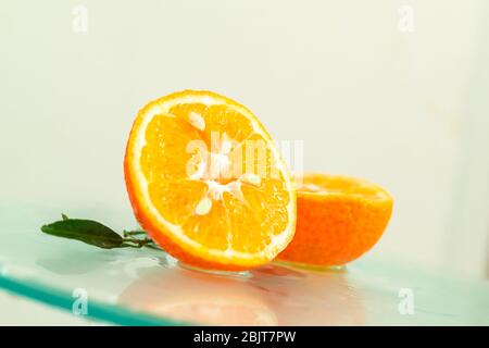 three orange tangerines with a branch and leaves stand in water on glass under drops of water on a white background copy space Stock Photo
