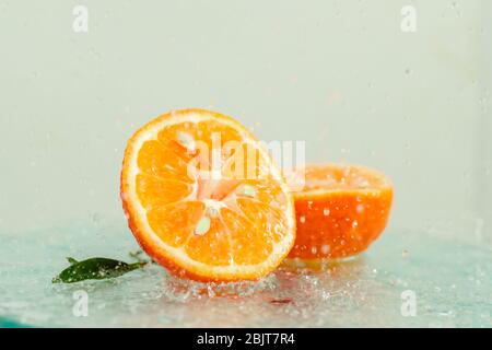 three orange tangerines with a branch and leaves stand in water on glass under drops of water on a white background copy space Stock Photo