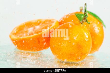 three orange tangerines with a branch and leaves stand in water on glass under drops of water on a white background Stock Photo