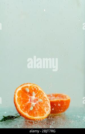 three orange tangerines with a branch and leaves stand in water on glass under drops of water on a white background copy space Stock Photo