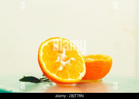 three orange tangerines with a branch and leaves stand in water on glass under drops of water on a white background copy space Stock Photo