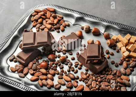 Tray with chocolate, hazelnuts, cocoa and coffee beans on table Stock Photo