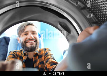 Man doing laundry in laundromat, view from the inside of washing machine Stock Photo