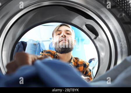 Man doing laundry in laundromat, view from the inside of washing machine Stock Photo