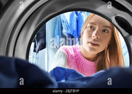 Young woman doing laundry in laundromat, view from the inside of washing machine Stock Photo