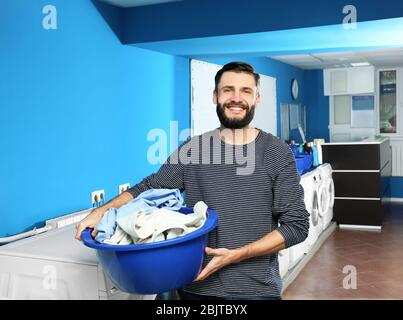 Young man with dirty clothes in laundromat. Laundry day Stock Photo