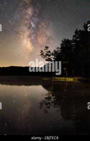 A lone tree reaches out over the glassy waters of Boley Lake behind the Milky Way at Babcock State Park, West Virginia. Stock Photo
