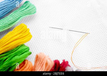 White fabric with colorful threads and sewing needle, closeup Stock Photo
