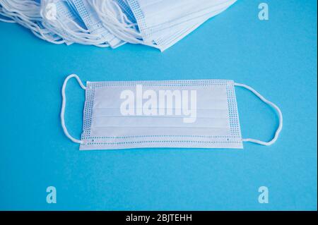 Surgical mask with rubber ear straps on blue background. Typical 3-ply surgical mask to cover the mouth and nose. Stock Photo