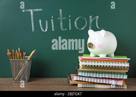 Chalkboard with word TUITION and piggy bank on notebooks Stock Photo