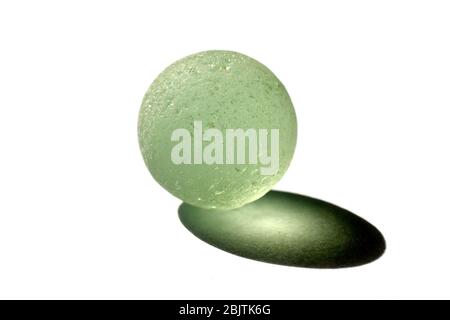 Close up still life of a chipped pale green glass marble and the shadow it casts in directional sunlight, isolated against a white background. Stock Photo