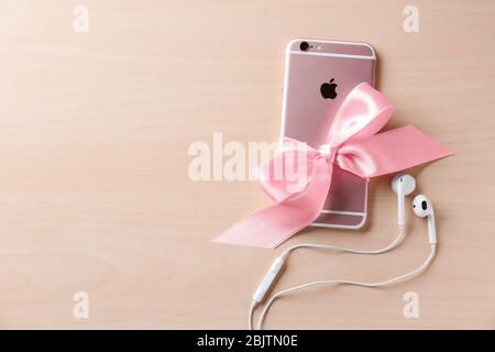 KYIV, UKRAINE - NOVEMBER 28, 2017: Modern iPhone 6s Plus Rose Gold with bow and earpods on wooden background Stock Photo