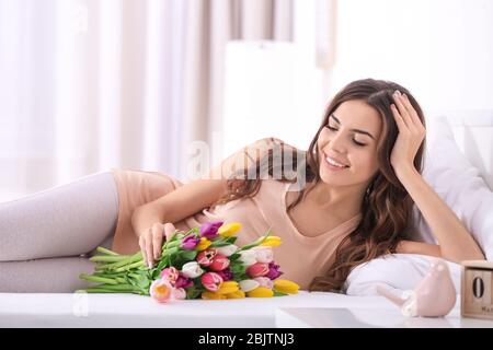 Beautiful woman with bouquet of tulips on bed at home Stock Photo