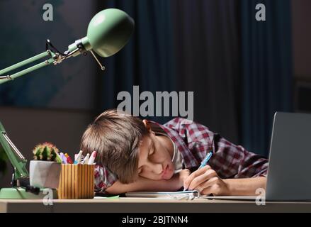 Teenager falling asleep while doing homework at table in evening Stock Photo