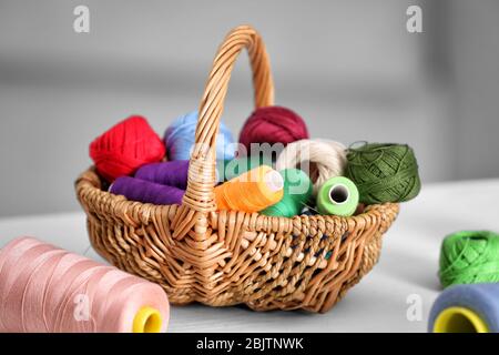 Set of colorful threads for sewing and crocheting in wicker basket on table Stock Photo