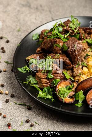 Stewed beef with mushrooms and a side dish of lentils on a black plate. Close-up Stock Photo