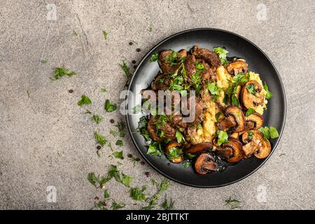 Stewed beef with mushrooms and a side dish of lentils on a black plate. Top view with place for text. Stock Photo