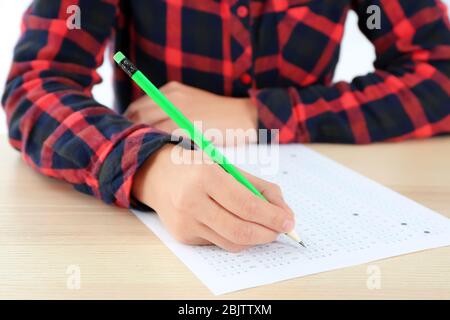 Student choosing answers in test form to pass exam at table Stock Photo