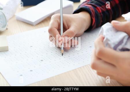 Student choosing answers in test form to pass exam at table Stock Photo