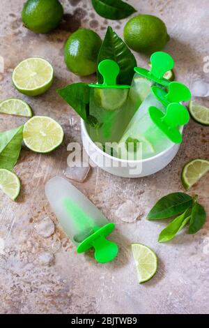 Homemade popsicles with lime juice and mint, mojito fruit ice on a light stone or slate background. Copy space. Stock Photo