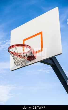 A basketball backboard, rim and net on a playground against a blue sky. Stock Photo