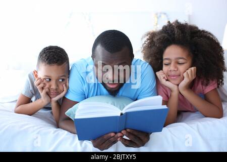 African American man reading bedtime story to his children on bed Stock Photo