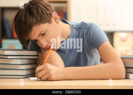 Tired teenager boy doing homework in library Stock Photo