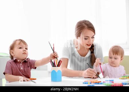 Cute little children drawing with young nanny, indoors Stock Photo