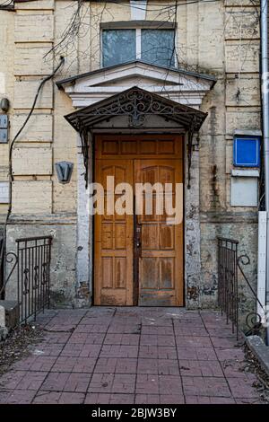 Antique ornate metal porch and aged wooden door in brick wall. Architectural details of yellow stone building. Stock Photo