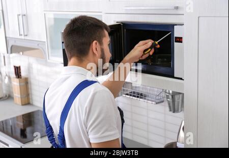 Young man repairing microwave oven in kitchen Stock Photo