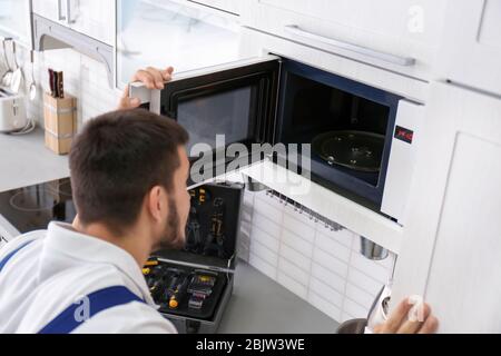 Young man repairing microwave oven in kitchen Stock Photo
