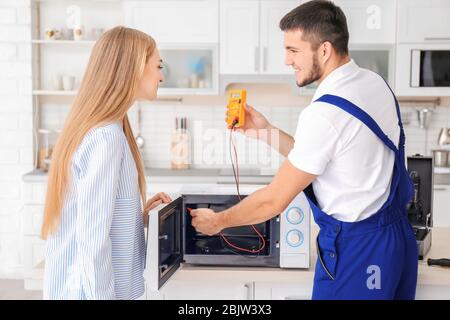 Housewife with worker near microwave oven in kitchen Stock Photo