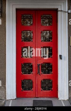 Retro style wooden doorway. Ornate red double door with rows of square shape windows and patterned metal gratings. Stock Photo
