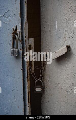 Obsolete padlocks on rusty chains closed old metal gates painted in grey color. Rough texture of old metal handle and uneven surface of gate Stock Photo