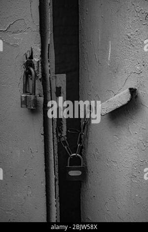Black and white photo of retro padlocks on rusty chains closed old metal gates painted in grey color. Rough texture of old metal handle and uneven sur Stock Photo