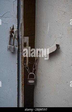 Closeup of retro padlocks on rusty chains closed old metal gates painted in grey color. Rough texture of old metal handle and uneven surface of gate Stock Photo