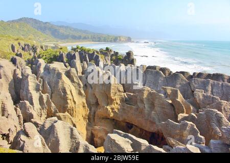 Scenic coast with wild rock formations called Pancake Rocks at Punakaiki in New Zealand with a nice long beach in the background. Stock Photo