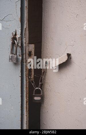 Grunge retro padlocks on rusty chains closed old metal gates painted in grey color. Rough texture of old metal handle and uneven surface of gate Stock Photo